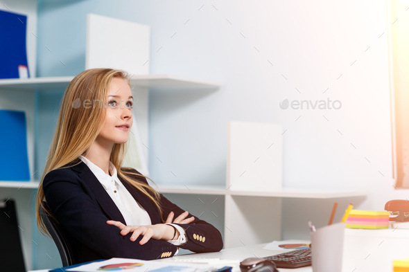 Young pretty business woman sitting at the desk with computer in blue office